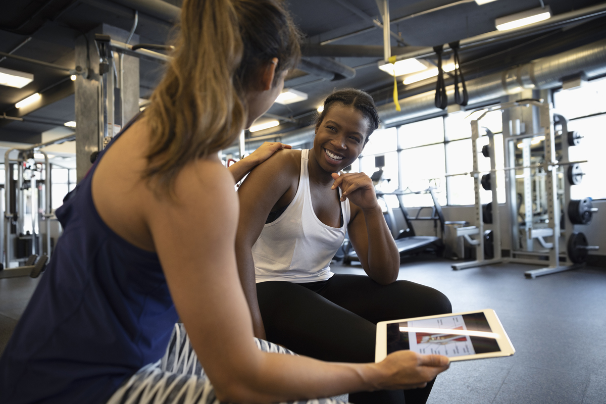 Two women in a gym setting talking about fitness goals.